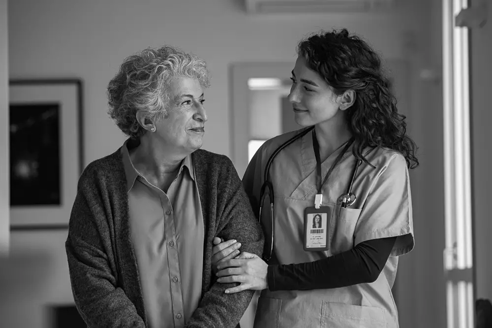 An older woman walks down the hallway with her nurse
